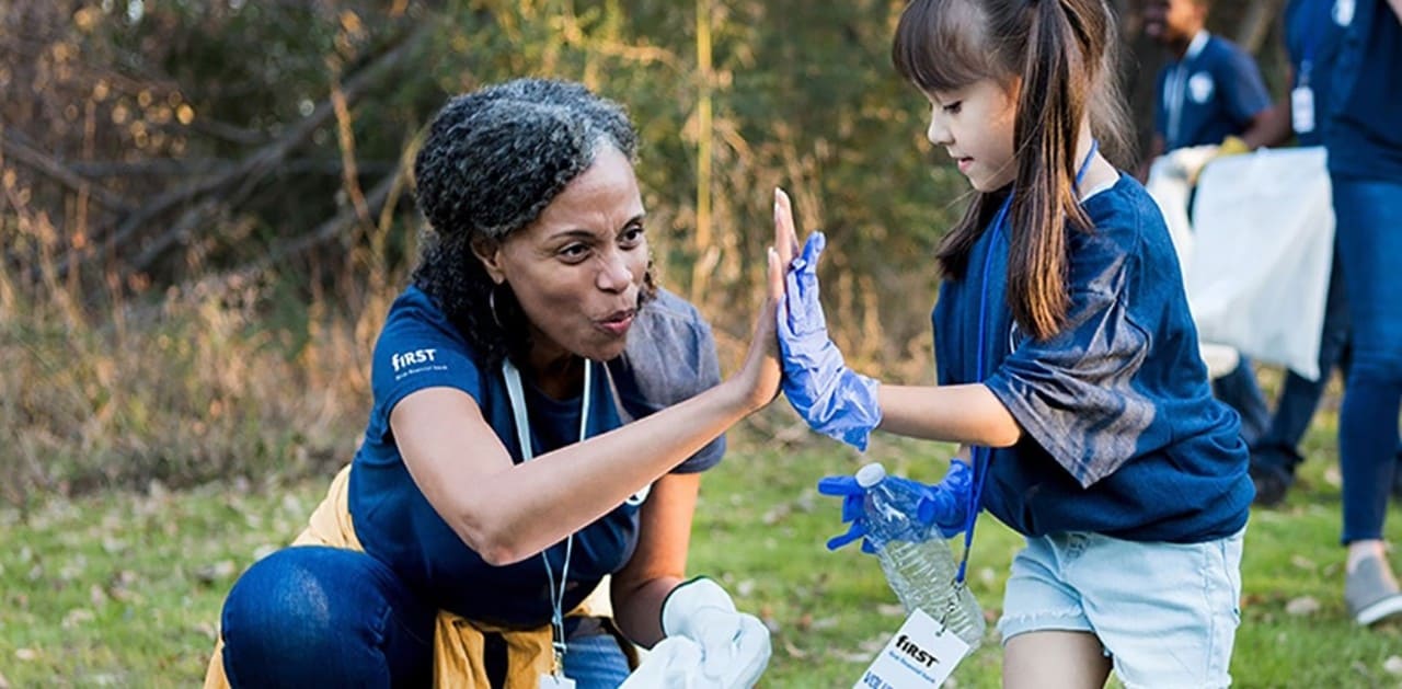 A woman high-fives a little girl as they pick up trash