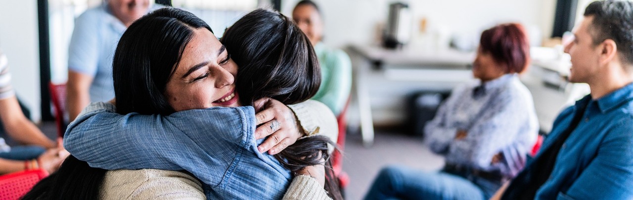 Two women hugging in a group discussion setting