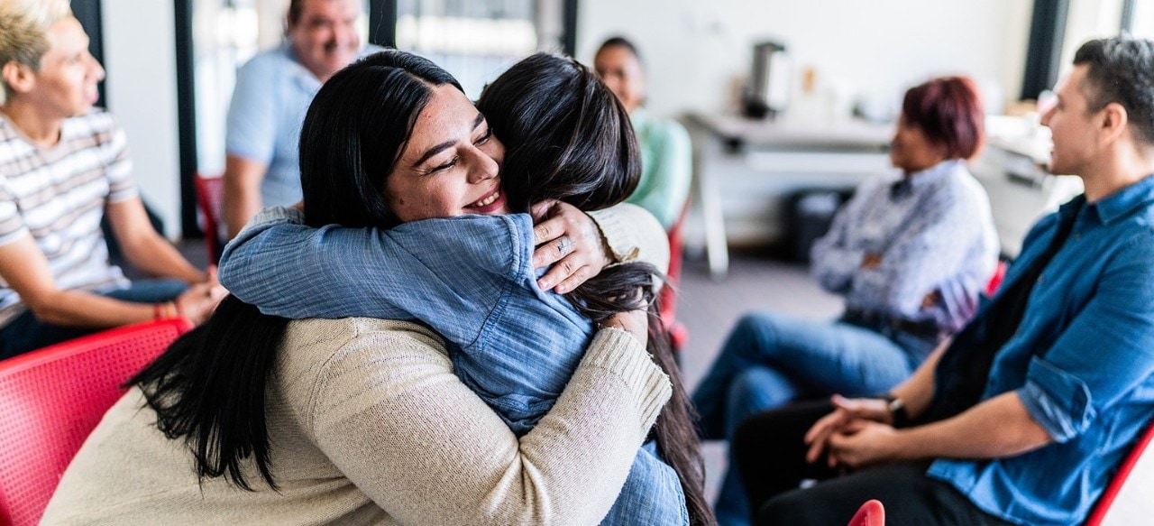 Two women hugging in a group discussion setting