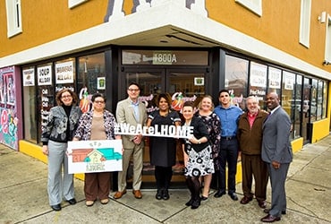 Diverse group of people holding a #WeAreLHOME sign and an LHOME sign