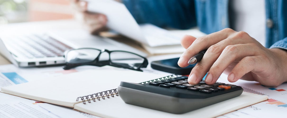 Man making financial calculations using calculator, laptop, and paper documents