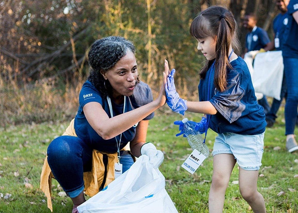 A woman high-fives a little girl as they pick up trash
