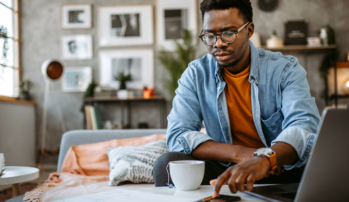African-American man using smartphone and laptop and drinking tea