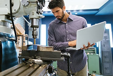 A man with a laptop looks over machinery