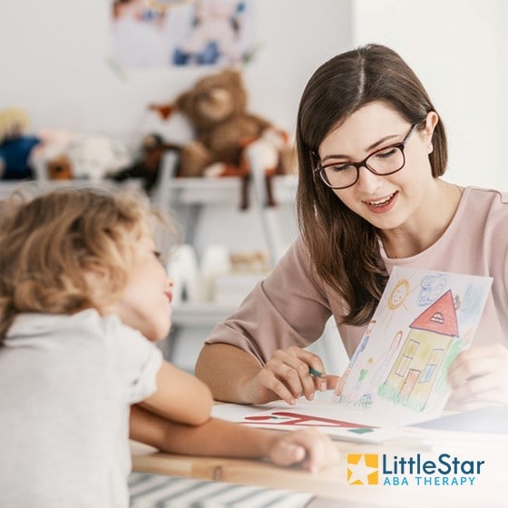 Woman and young girl looking at girl's drawing, with LittleStar ABA Therapy logo in corner