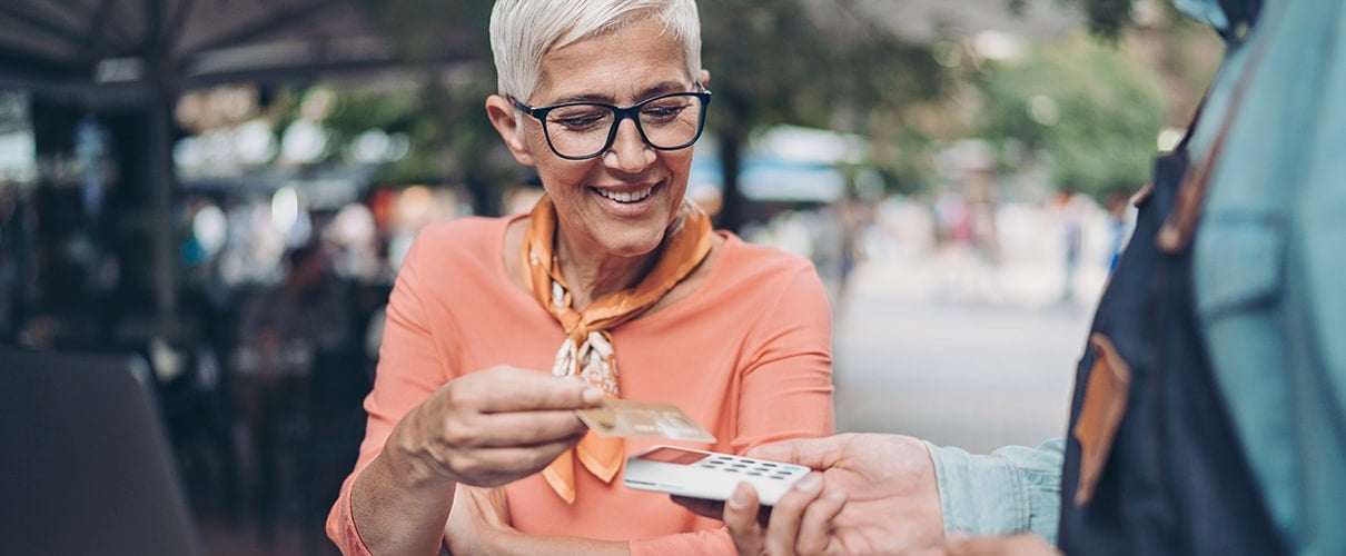 Smiling senior woman making a contactless payment at an outside restaurant