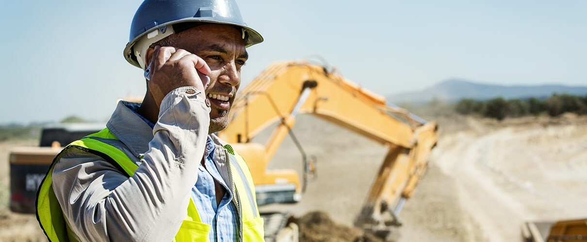 Hispanic construction foreman on phone with bulldozer in background