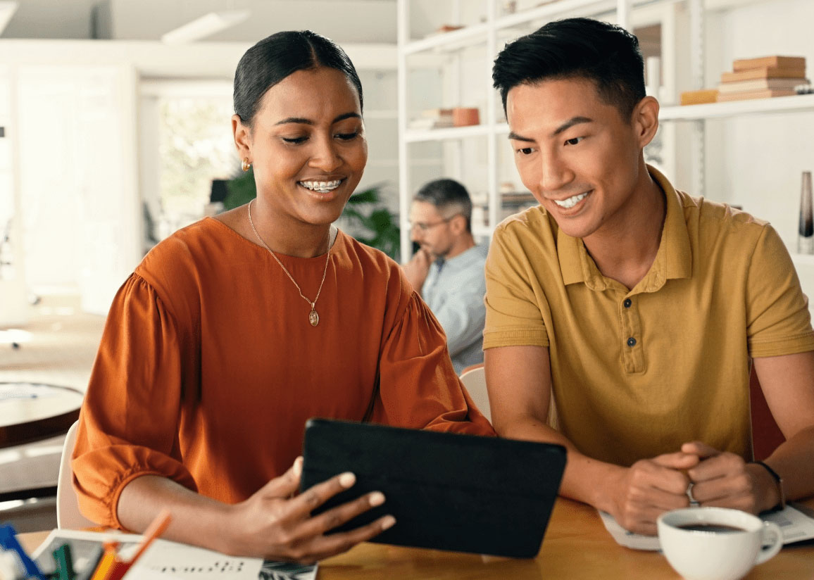 African-American woman and Asian man looking at tablet and drinking coffee