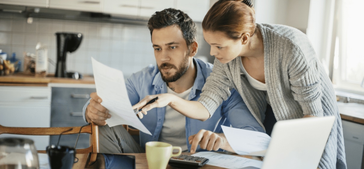 Man and woman using a calculator and laptop and reviewing documents