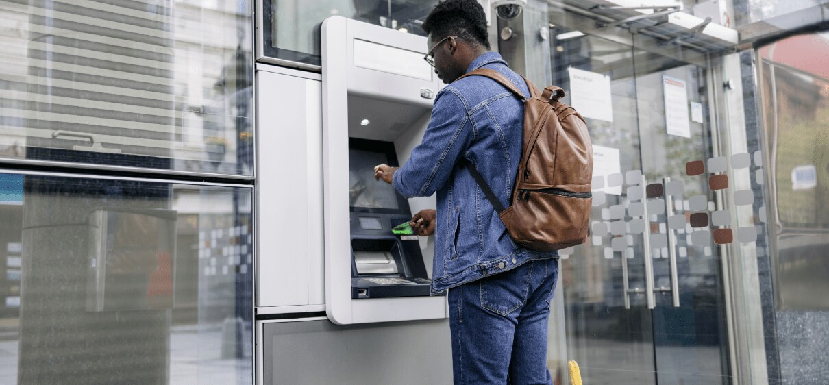 African-American man wearing backpack and using ATM