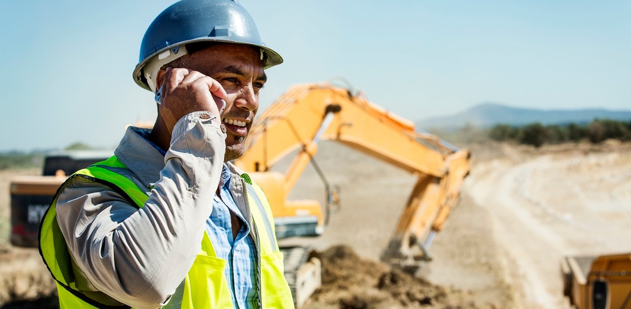 Hispanic construction foreman on phone with bulldozer in background