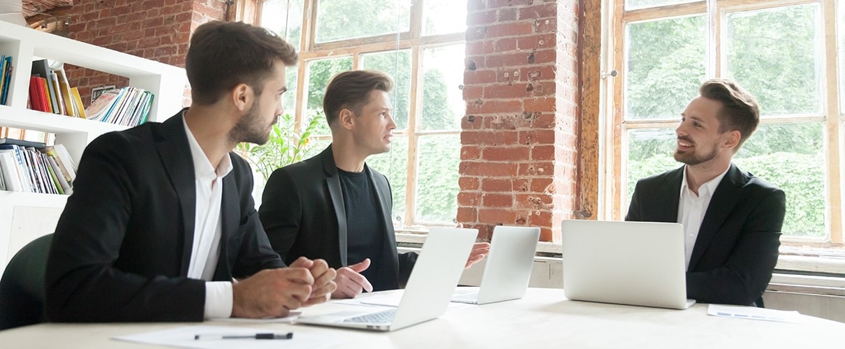 Three businessmen in suits negotiating discussing business sitting at conference office table at meeting