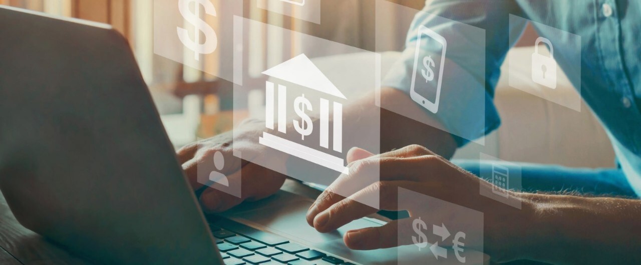 Hands working at laptop with superimposed financial icons floating in the air