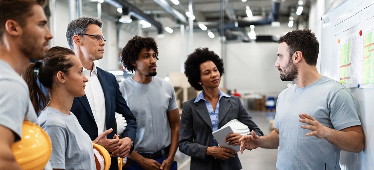 Young factory worker holding presentation about production development to company managers and his coworkers