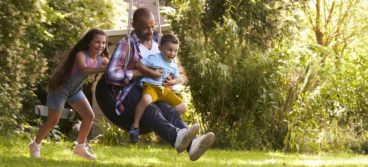 African-American girl pushing father and young brother on tire swing