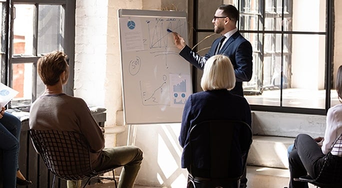 A man presenting financial data to colleagues on an easel pad