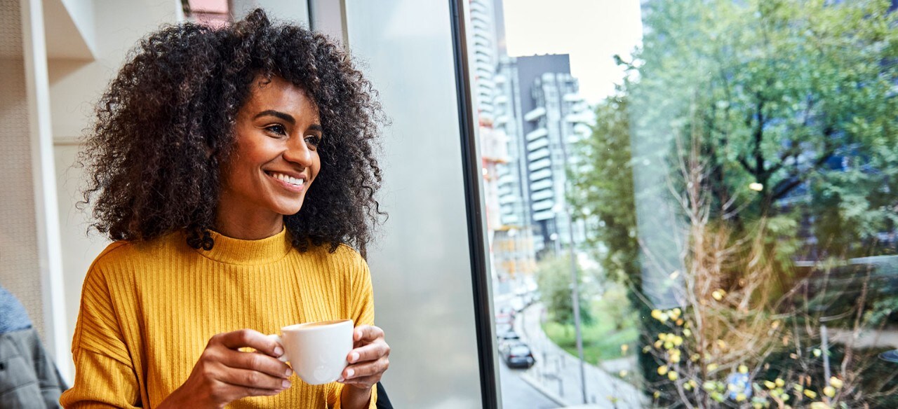 Smiling African-American woman holding coffee cup and looking out window
