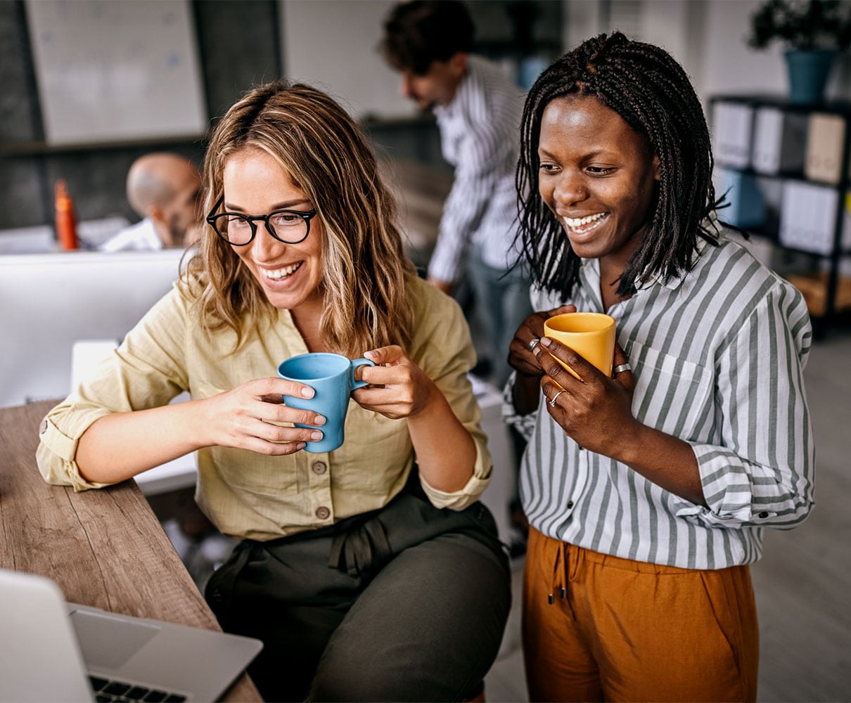 Two female colleagues smiling and holding coffee cups