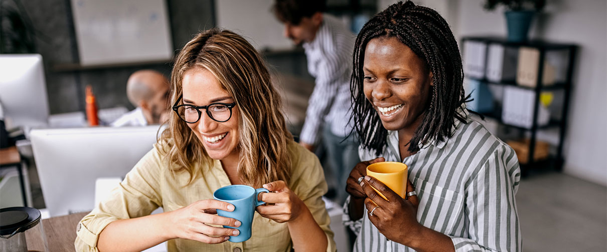 Two female colleagues smiling and holding coffee cups