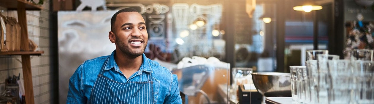 African-American coffee shop owner wearing apron and smiling behind counter