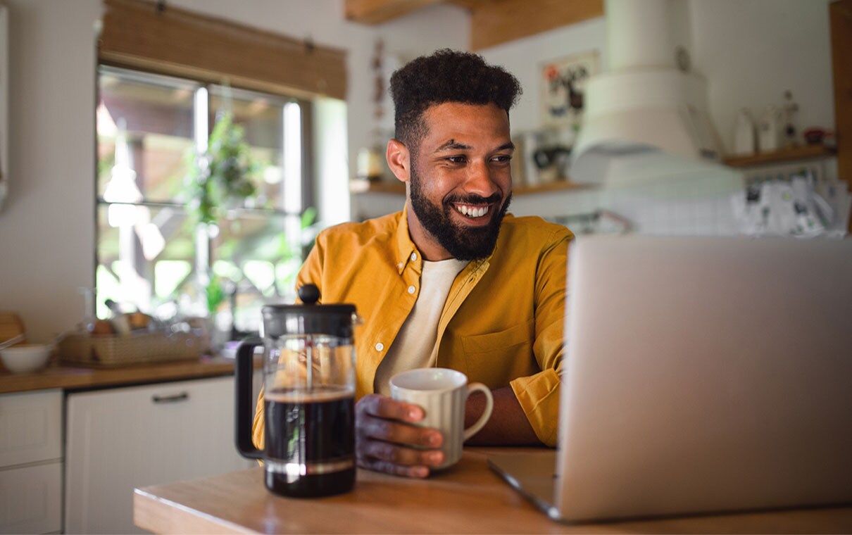Smiling African-American man drinking coffee and looking at laptop