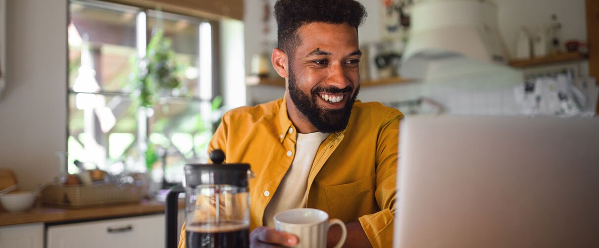 Smiling African-American man drinking coffee and looking at laptop