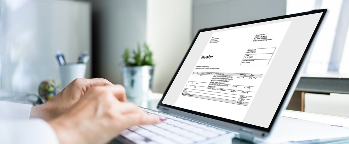 Close-up of a woman's hands typing on a laptop displaying an invoice