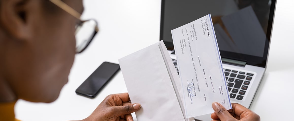 Woman removing a check from an envelope with a laptop and smartphone on her desk