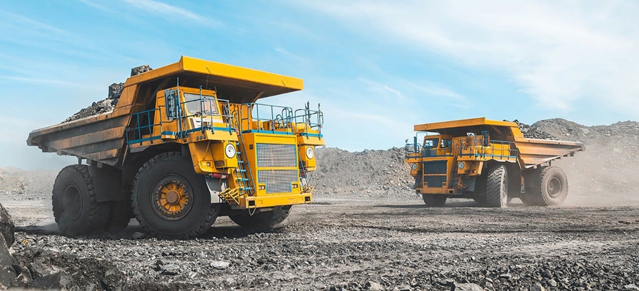 Two large construction dump trucks driving on rocky surface