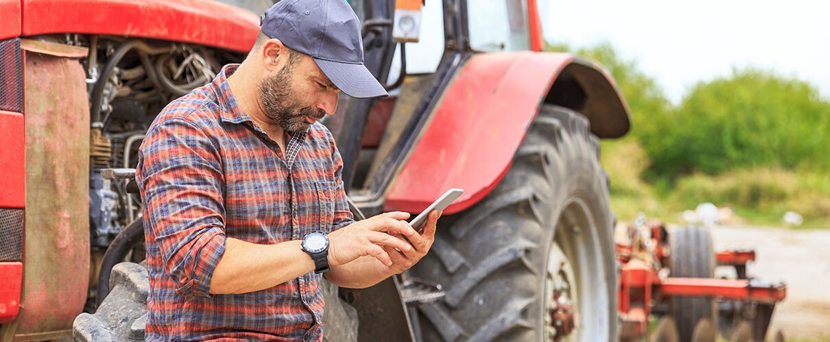 Farmer next to tractor looking at smartphone