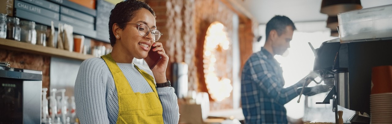 Happy female African-American coffee shop owner taking phone order