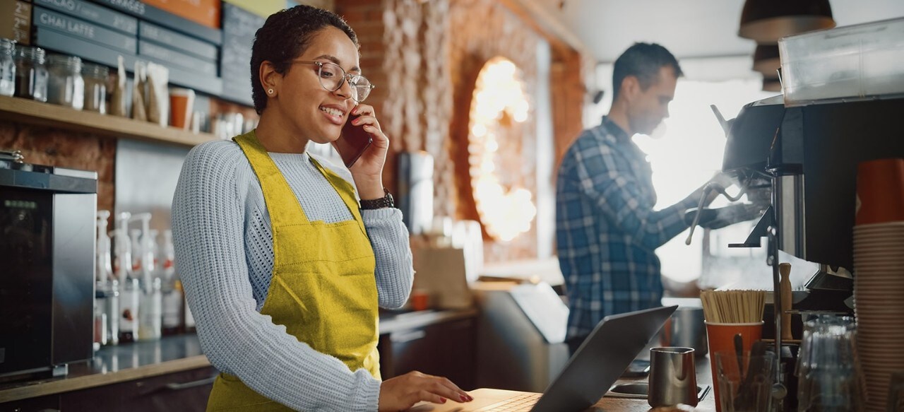 Happy female African-American coffee shop owner taking phone order