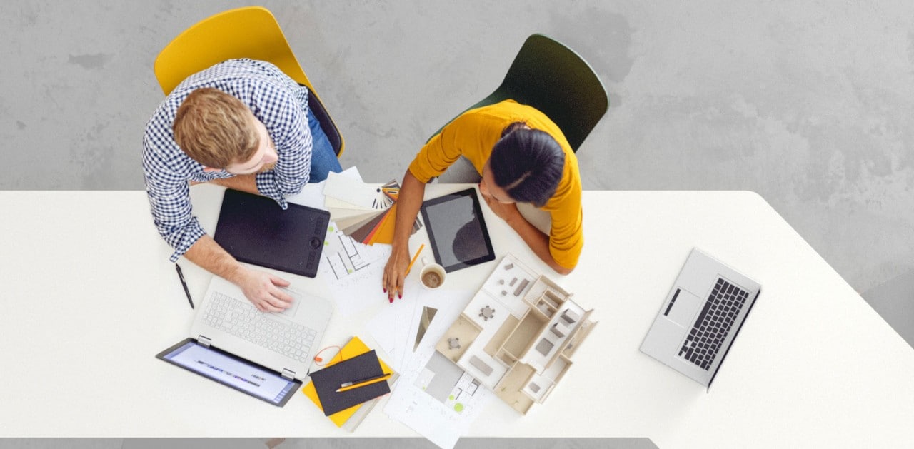 Overhead view of two colleagues at conference table with laptops and documents