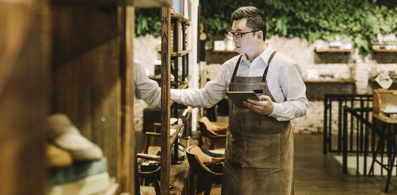 Asian-American male business owner holding tablet and checking inventory