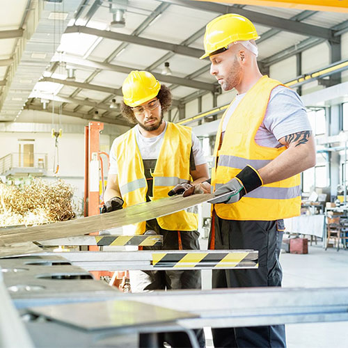 Two men in hard hats and high-visibility vests working in a manufacturing facility