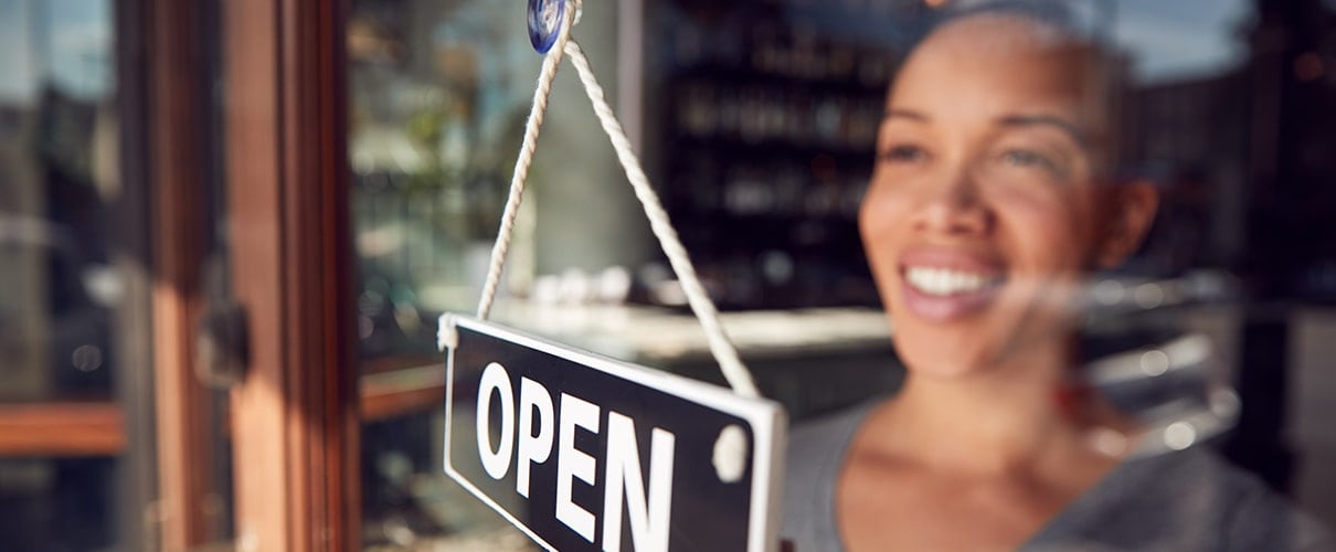 African-American coffee shop owner hanging “open” sign 