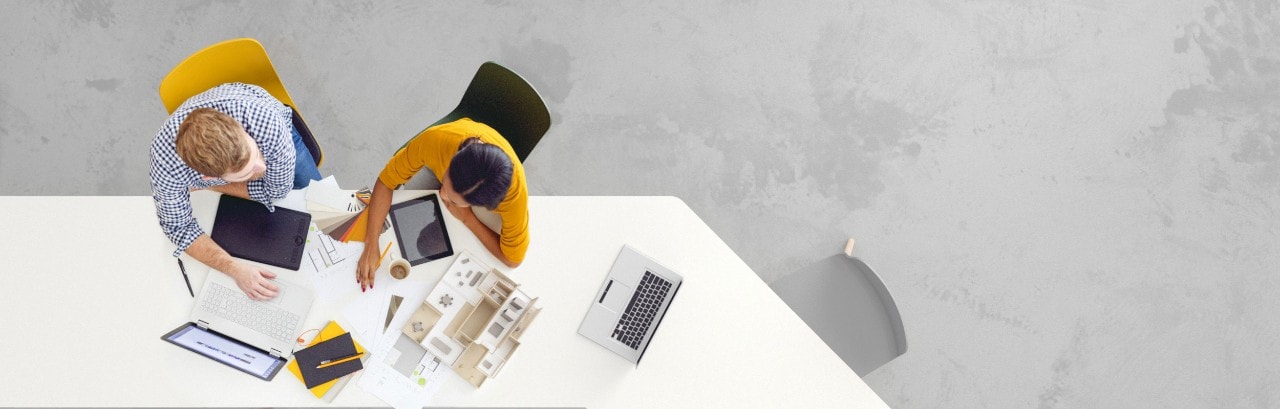 Overhead view of two colleagues at conference table with laptops and documents