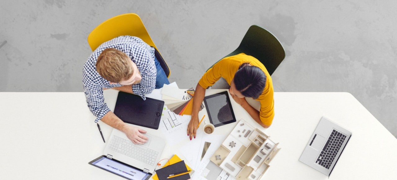 Overhead view of two colleagues at conference table with laptops and documents