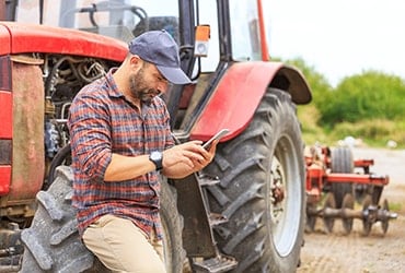 Farmer leaning against commercial tractor looking at smartphone