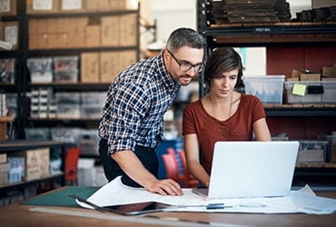 Male and female business partners looking at laptop in storage facility