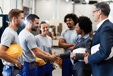 Employees with hard hats meeting with bankers in warehouse facility