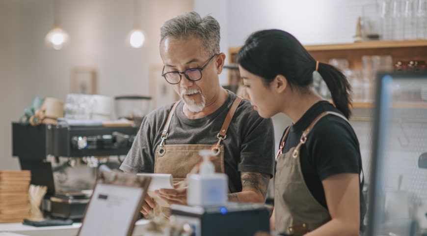 Father and daughter wearing aprons behind the counter of a coffee shop