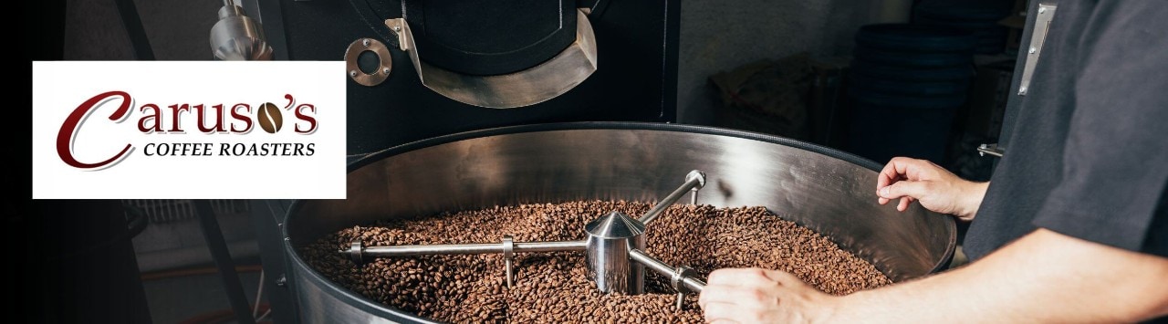 A person observes coffee beans roasting in high-capacity drum with Caruso's Coffee Roasters logo