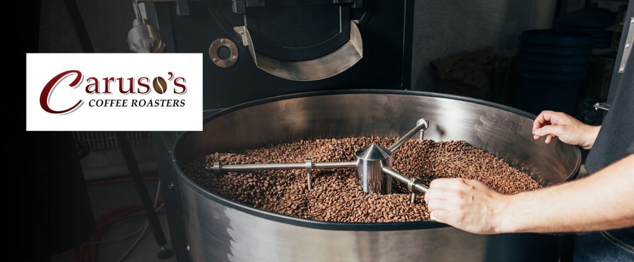 A person observes coffee beans roasting in high-capacity drum with Caruso's Coffee Roasters logo