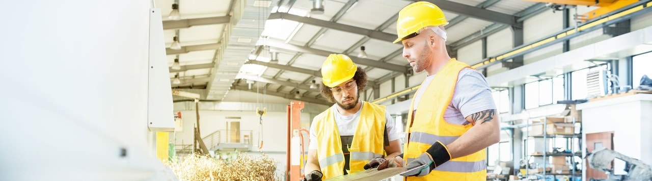 Two men in hard hats and high-visibility vests working in a manufacturing facility