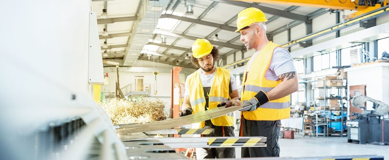 Two men in hard hats and high-visibility vests working in a manufacturing facility