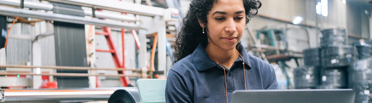 Female business owner working on laptop in front of manufacturing equipment