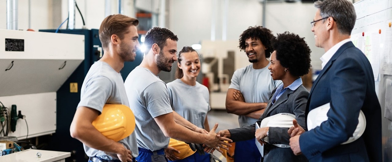 Employees with hard hats meeting with bankers in warehouse facility