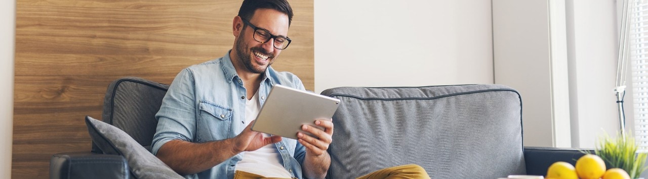 Happy man sitting on sofa looking at tablet