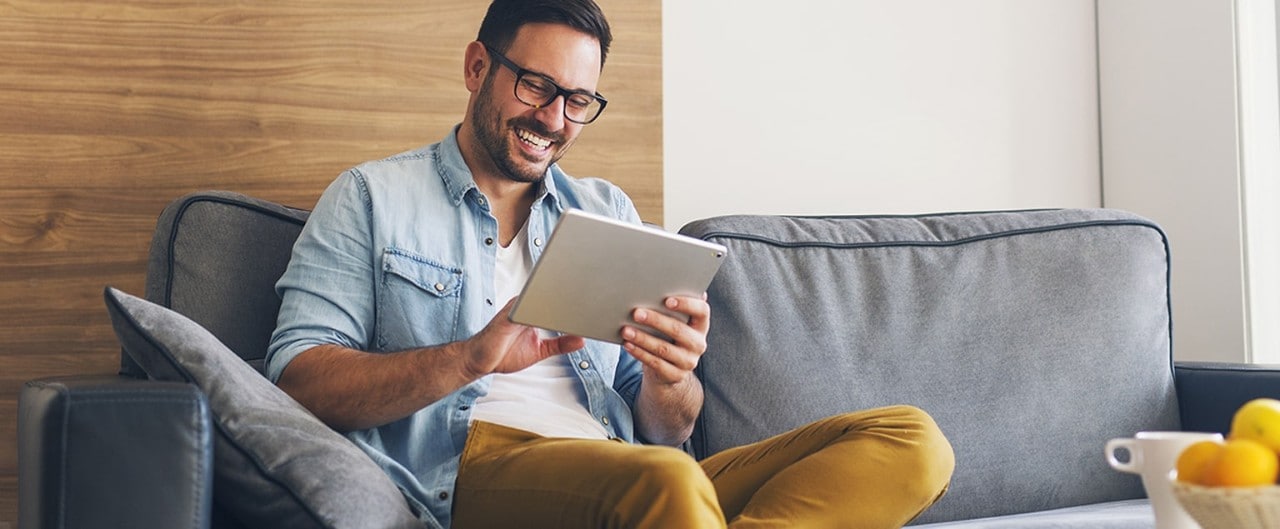 Happy man sitting on sofa looking at tablet